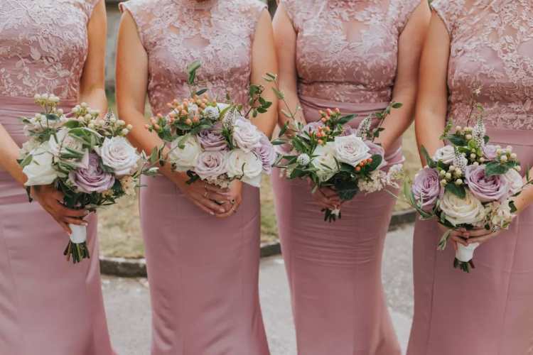 Bridesmaids in mauve pink dresses holding their bouquets.