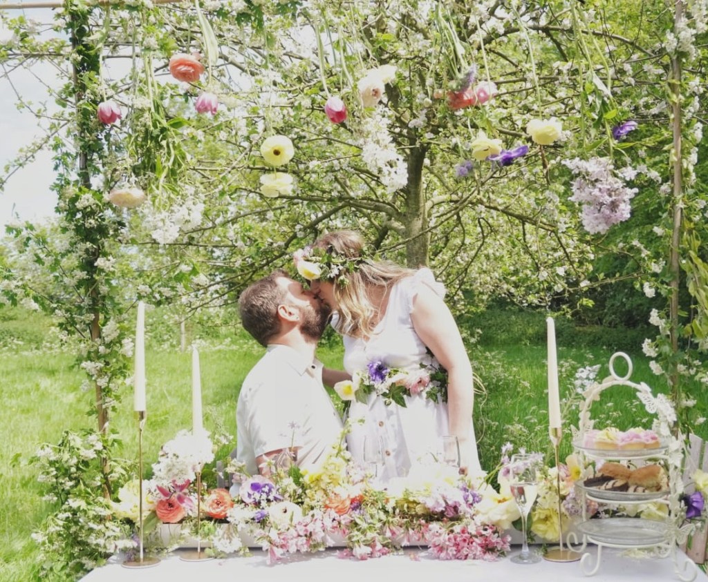 Couple kissing under a flower arch over their top table with floral table runner
