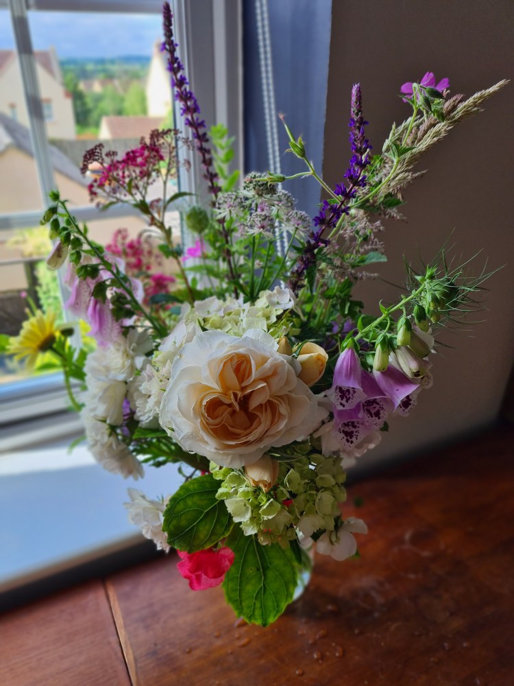 A bouquet of british flowers filled with roses, foxgloves, verbena, geranium, herbs, and sweetpeas