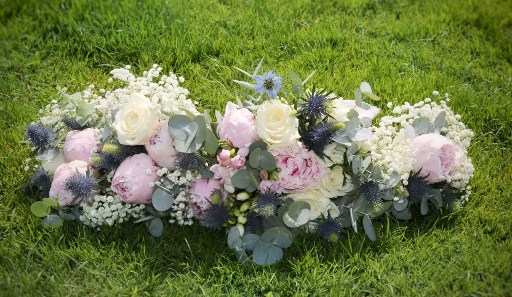 Bridal and bridesmaids bouquets with white roses, pink peonies, blue sea holly, blue nigella, eucalyptus, gypsophila, and white freesias