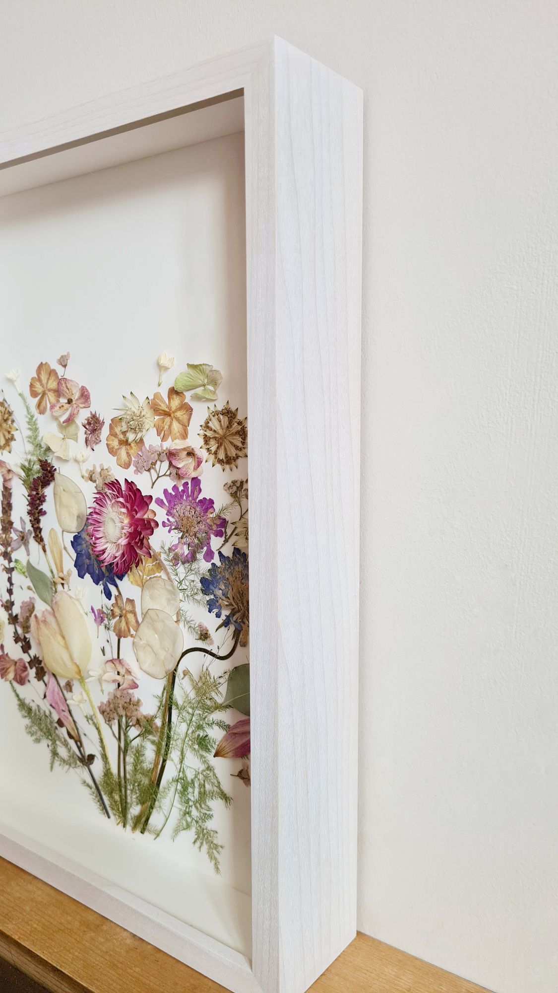 Flower preservation artwork, with pressed and 3D dried flowers on a museum grade frame with anti reflective glass, UV protected glass, and white back board and white frame surround.