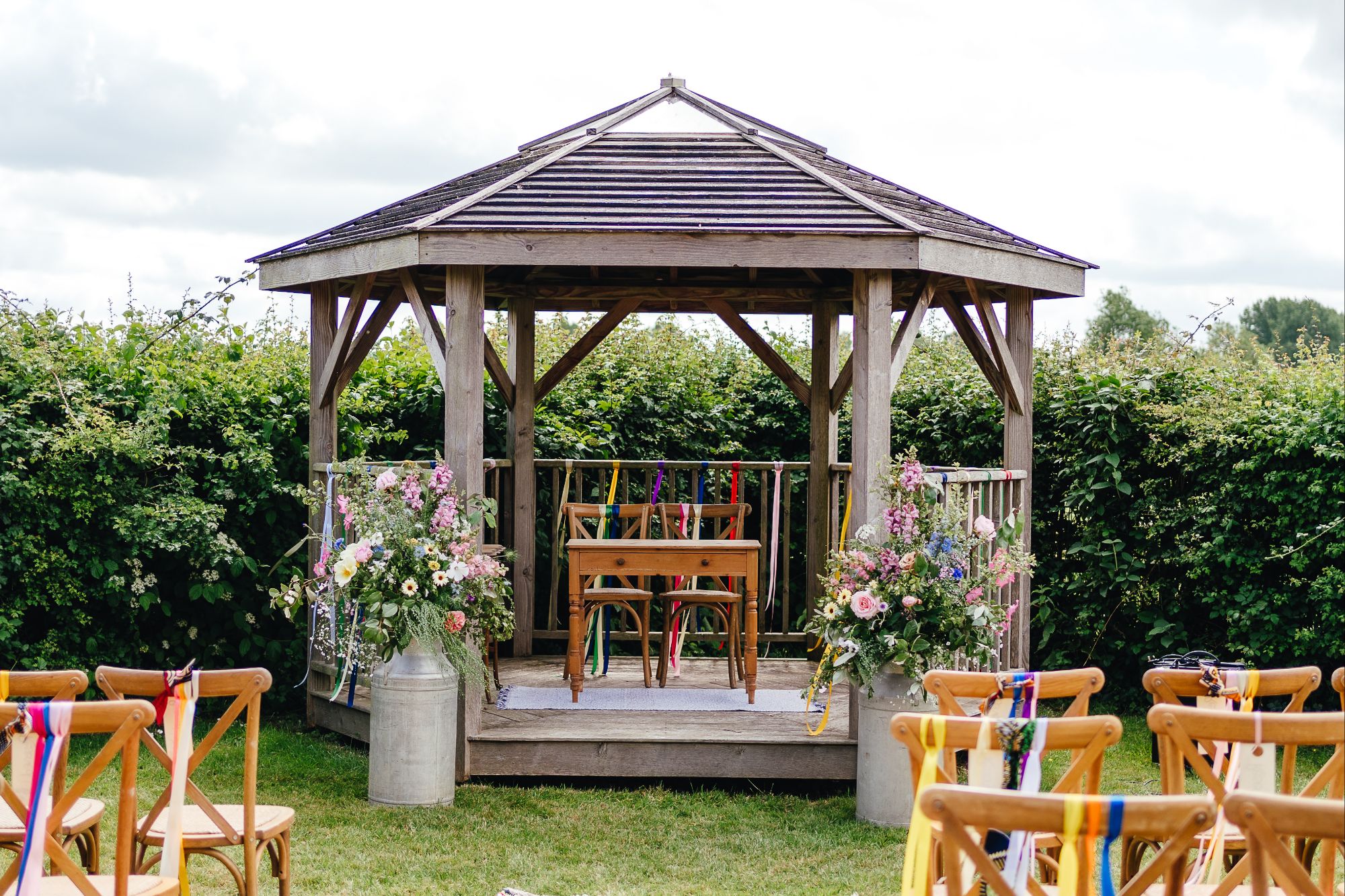 Floral milk churns either side of the wedding ceremony pergola, for a tipi festival wedding at Pennard Hill Farm in Somerset, right before Glastonbury Festival