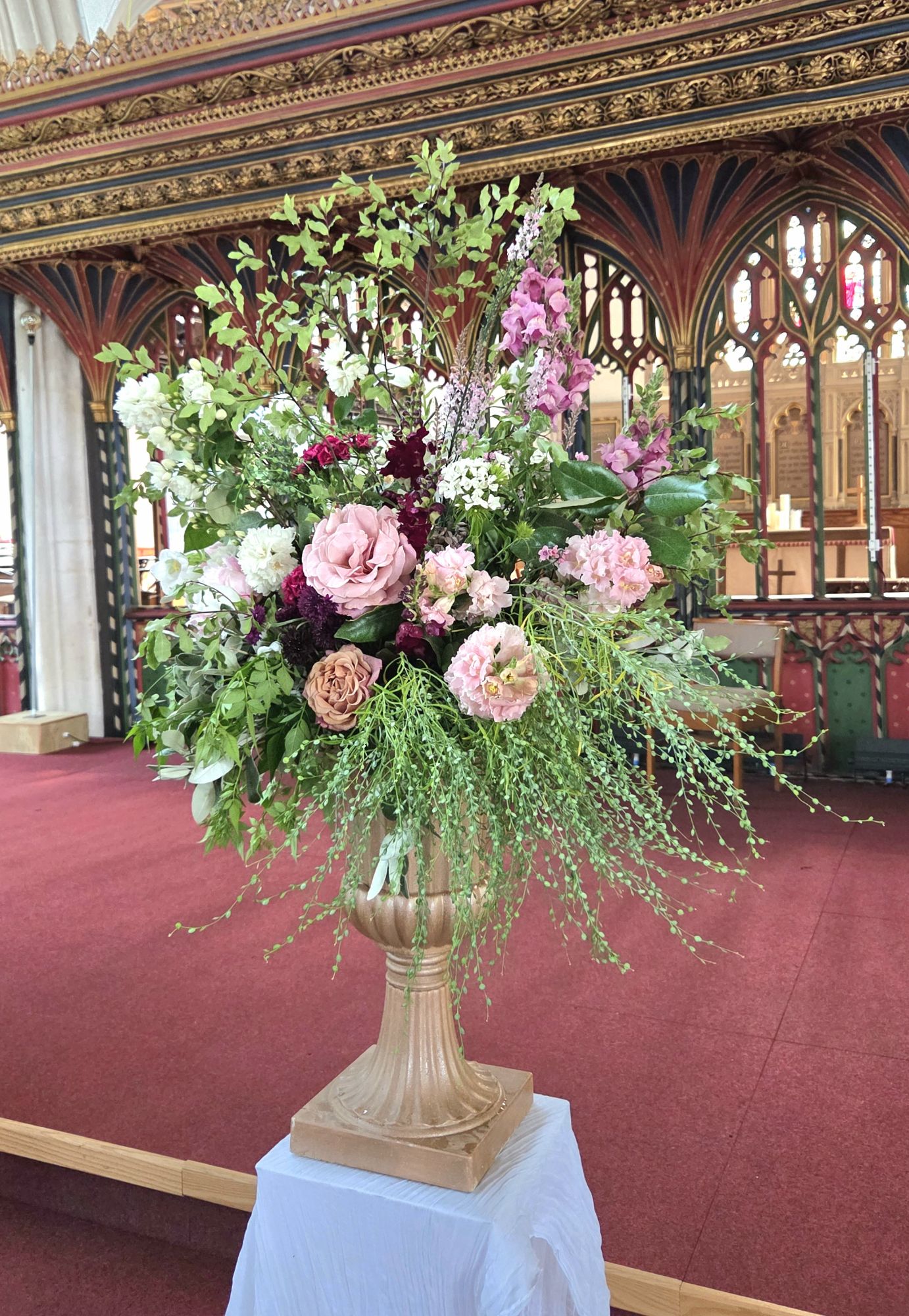 Pale pinks and mauves wedding floral urn on plinth in church