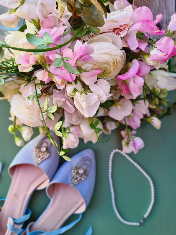 Pink sweet peas and ranunculus in a spring wedding bouquet with blue bridal shoes
