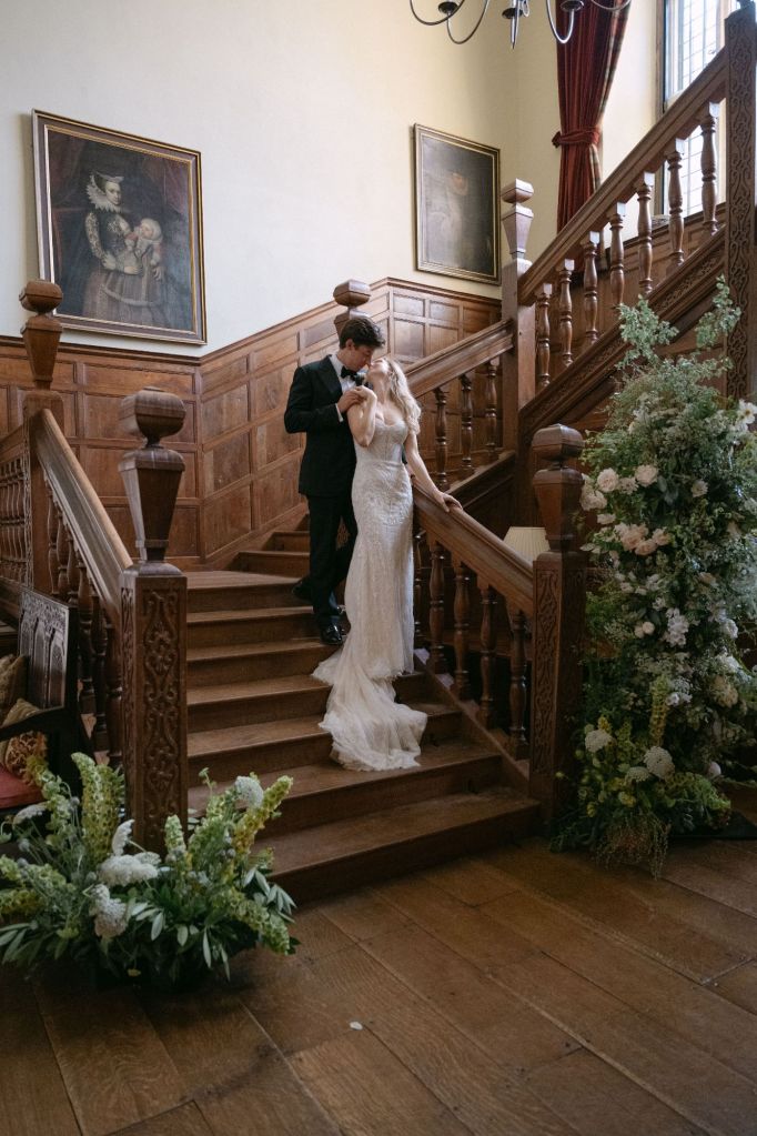 Bride and Groom on the stairs at North Cadbury Court in Somerset, surrounded by wedding flowers by The Honey Seeker Floral Design