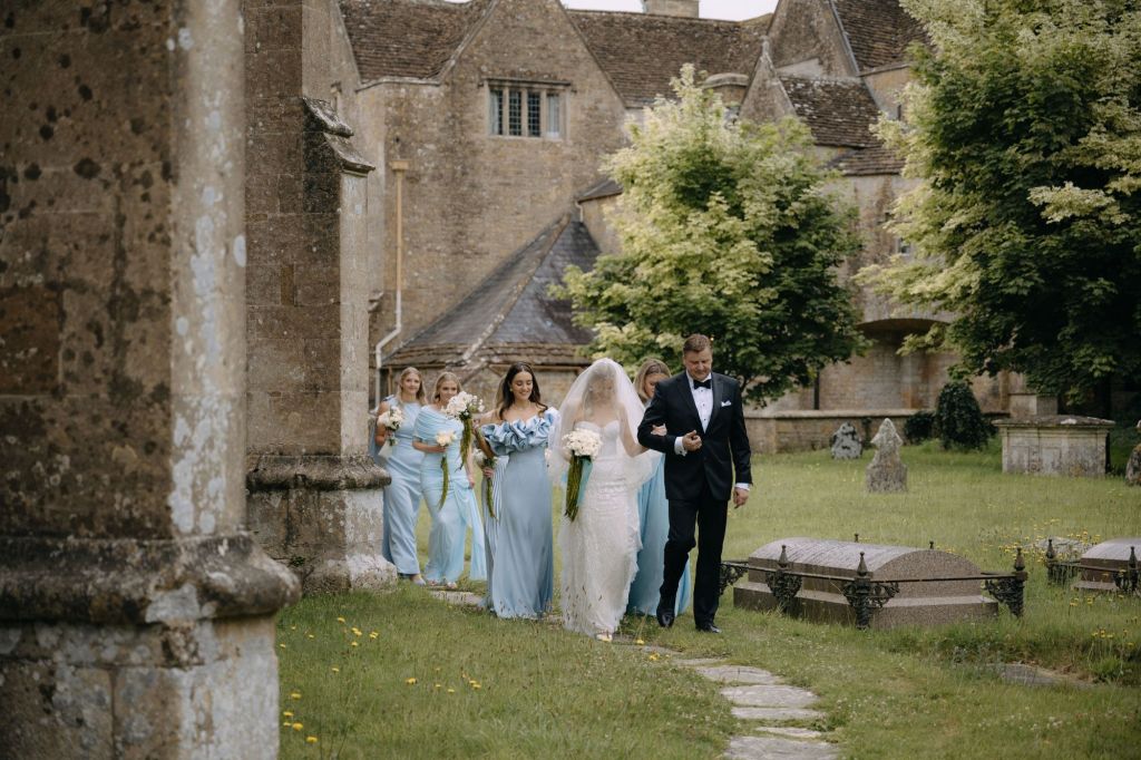 Bride and Bridal party walking around St. Mary's church at North Cadbury Court in Somerset, on the way to the wedding ceremony, flowers by The Honey Seeker Floral Design