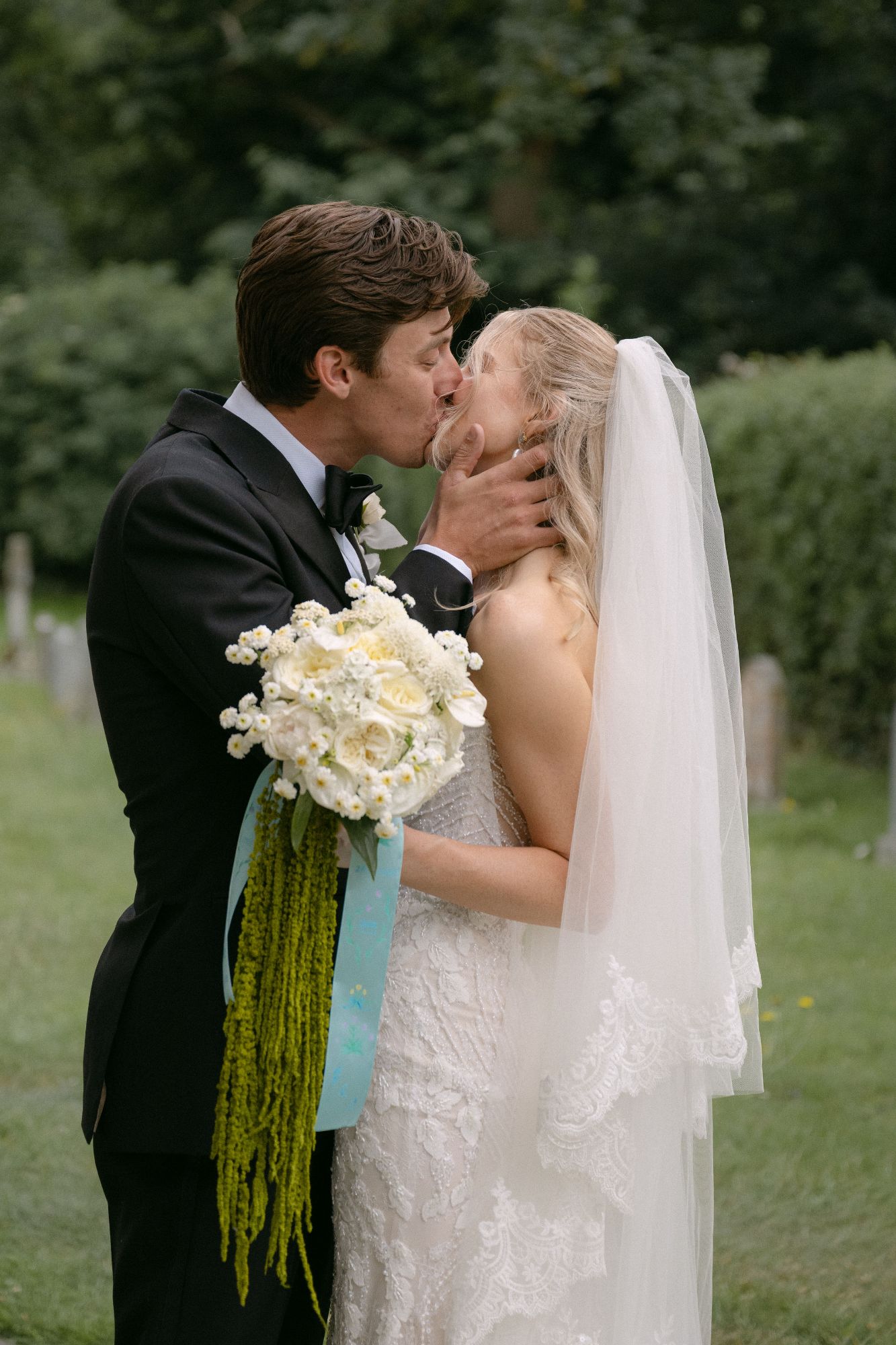 Bride and groom kiss, bride holding her white bouquet by The Honey Seeker Floral Design in Somerset, North Cadbury Court, photo: Sophia Veres