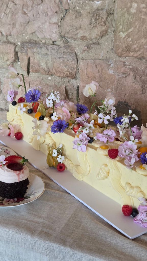 Wedding cake, log cake, long cake, covered in spring flowers and fruit