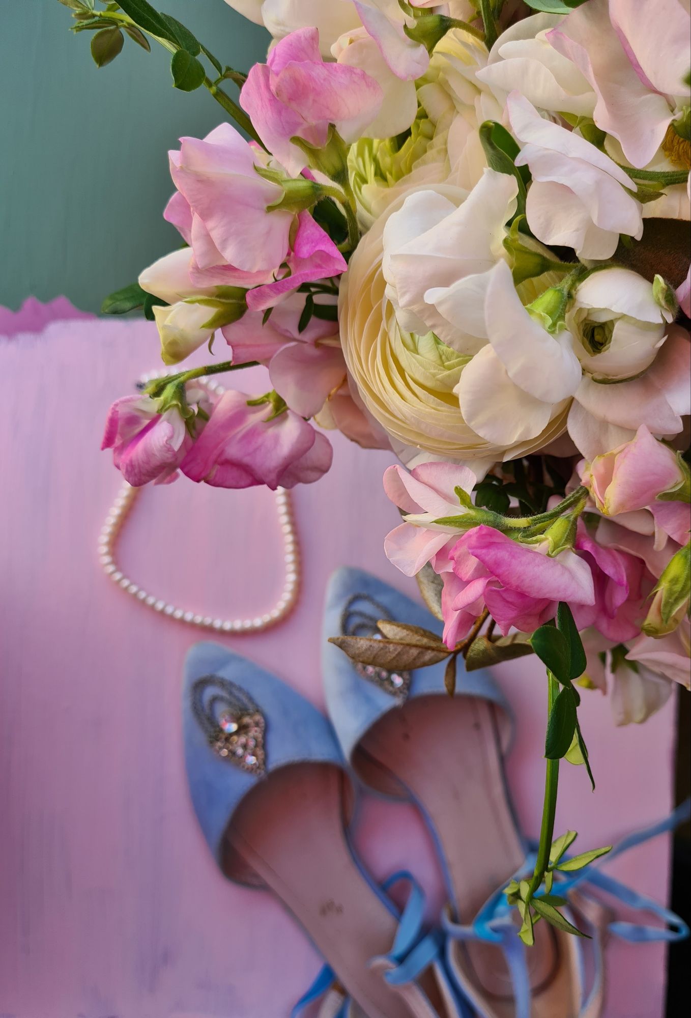 Blue wedding shoes with spring wedding flowers in pinks and creams, frilly sweet peas and ranunculus on a backdrop of pink and green